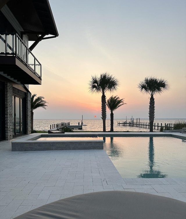 pool at dusk featuring a jacuzzi and a water view