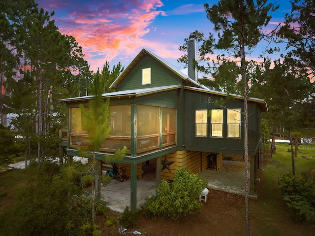 back house at dusk featuring a sunroom and a patio area