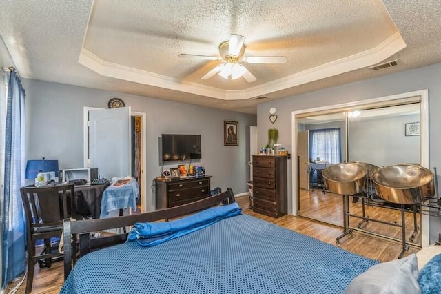 bedroom with ceiling fan, a tray ceiling, a textured ceiling, and wood-type flooring