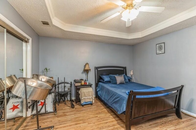 bedroom with a tray ceiling, a textured ceiling, ceiling fan, and light hardwood / wood-style flooring