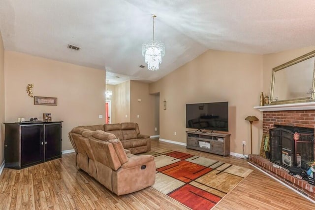 living room with a brick fireplace, a chandelier, and hardwood / wood-style flooring