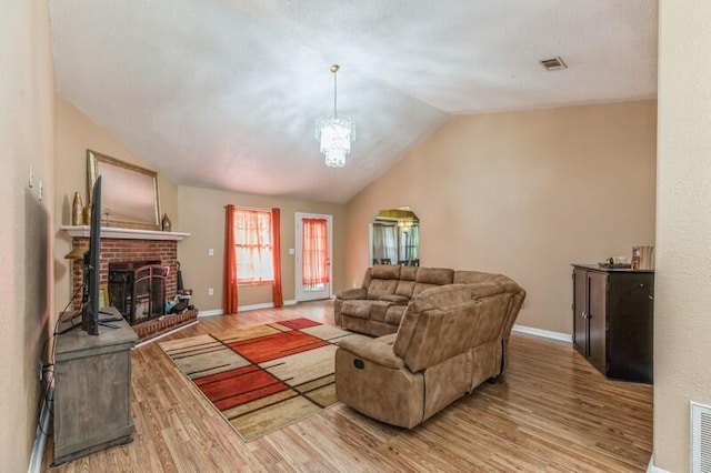 living room featuring a brick fireplace, vaulted ceiling, an inviting chandelier, and wood-type flooring