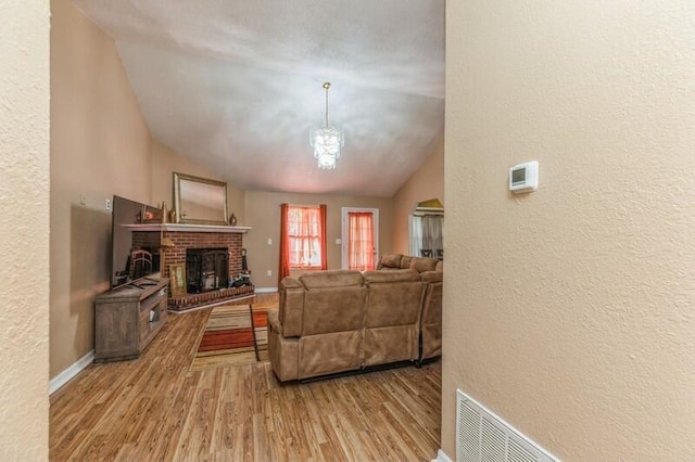 living room featuring vaulted ceiling, hardwood / wood-style floors, and a brick fireplace