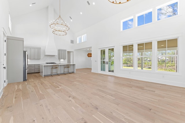 unfurnished living room with light wood finished floors, visible vents, baseboards, a high ceiling, and a chandelier