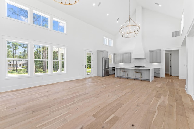 unfurnished living room featuring a notable chandelier, baseboards, visible vents, and light wood-style floors