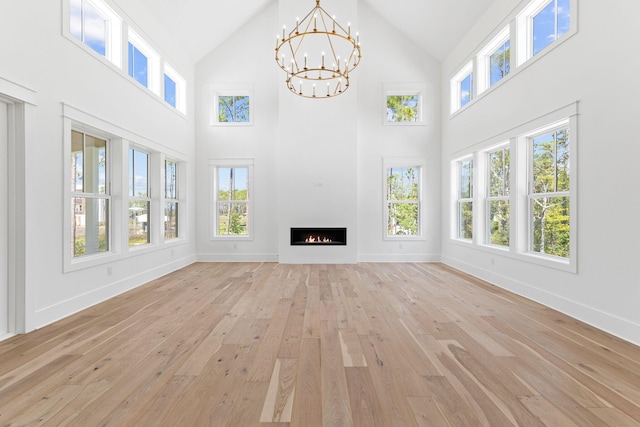 unfurnished living room with light wood-type flooring, a healthy amount of sunlight, a lit fireplace, and an inviting chandelier