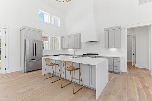 kitchen with a kitchen island with sink, gray cabinetry, a sink, a kitchen breakfast bar, and stainless steel fridge