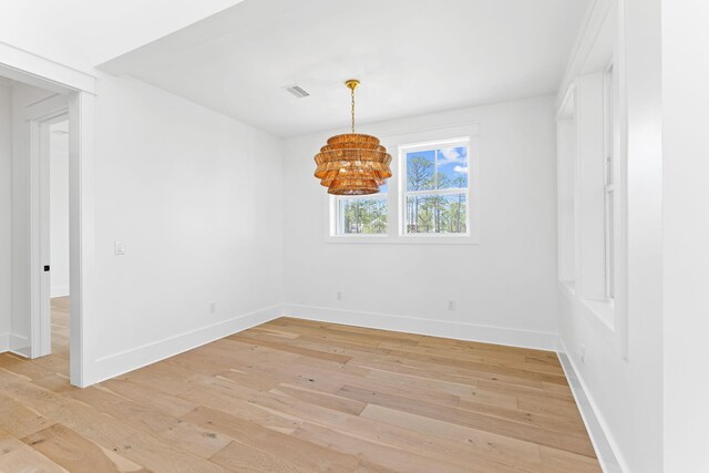 empty room with light wood-style floors, visible vents, baseboards, and an inviting chandelier