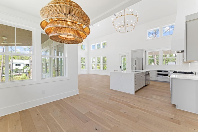 kitchen featuring light wood-style flooring, a kitchen island with sink, appliances with stainless steel finishes, and pendant lighting