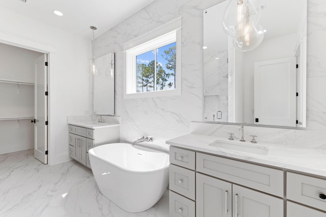 bathroom with a sink, marble finish floor, a spacious closet, a freestanding tub, and two vanities