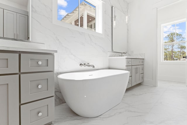 bathroom featuring stone wall, vanity, a freestanding bath, marble finish floor, and a closet