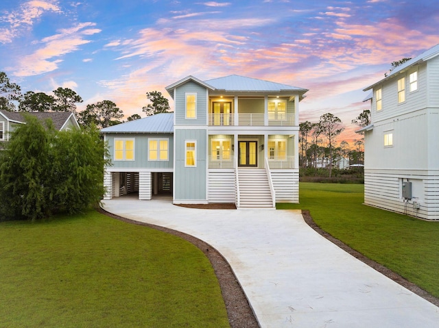 109 W Nursery Rd, Santa Rosa Beach, FL 32459 - back of house at dusk featuring a balcony, concrete driveway, metal roof, a lawn, and stairway