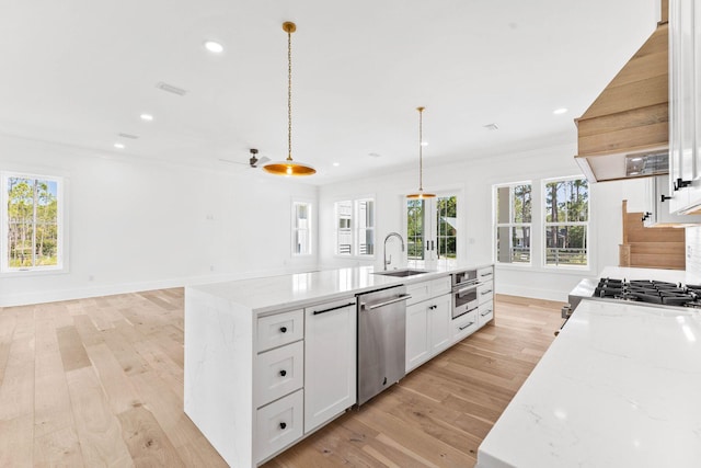 kitchen with white cabinetry, light hardwood / wood-style floors, appliances with stainless steel finishes, pendant lighting, and a center island with sink