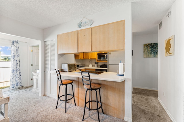 kitchen with a textured ceiling, white refrigerator, stainless steel microwave, kitchen peninsula, and light colored carpet