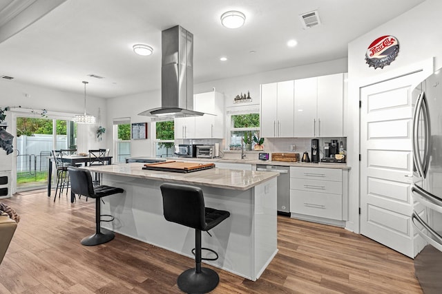 kitchen with a kitchen island, island range hood, hardwood / wood-style flooring, white cabinetry, and appliances with stainless steel finishes