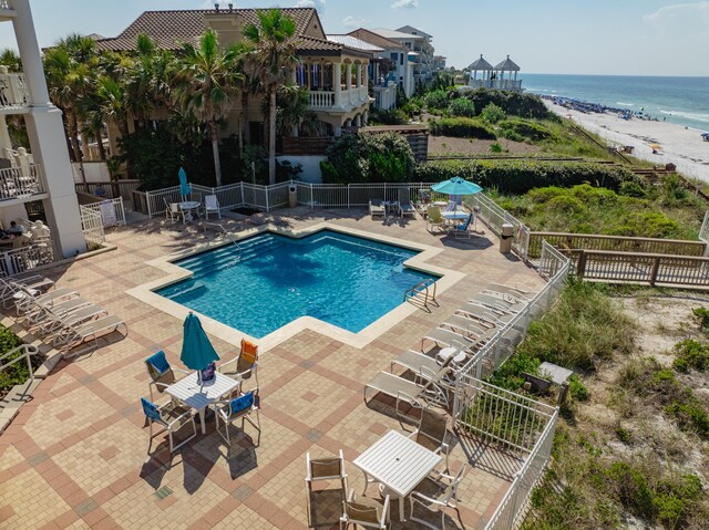 view of swimming pool featuring a water view, a beach view, and a patio