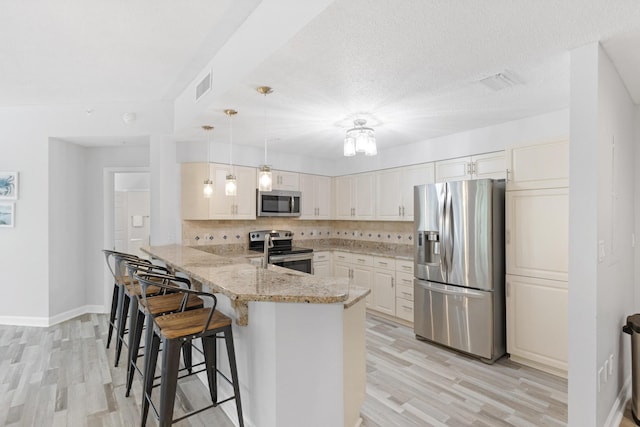 kitchen featuring a breakfast bar area, decorative light fixtures, light stone counters, kitchen peninsula, and stainless steel appliances