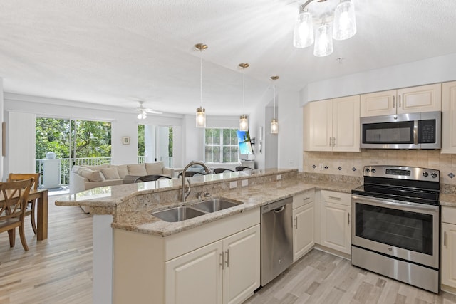 kitchen with light stone counters, sink, stainless steel appliances, and decorative light fixtures