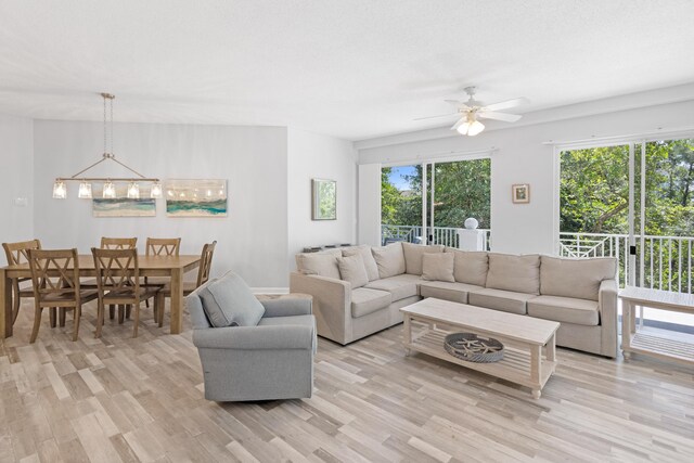 living room with ceiling fan with notable chandelier and light hardwood / wood-style flooring