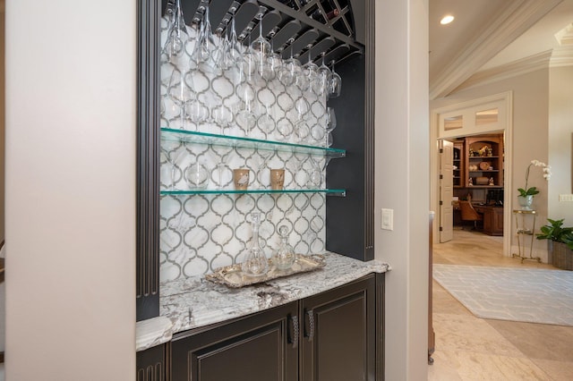 bar with dark brown cabinetry, light stone counters, and ornamental molding