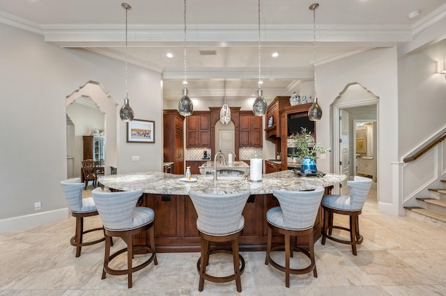 kitchen featuring ornamental molding, decorative light fixtures, light stone counters, and a large island