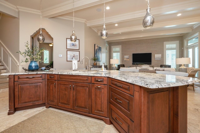 kitchen with light stone countertops, a kitchen island with sink, sink, beam ceiling, and decorative light fixtures