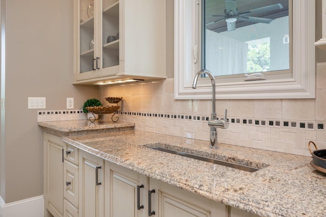 kitchen featuring ceiling fan, light stone counters, sink, and tasteful backsplash