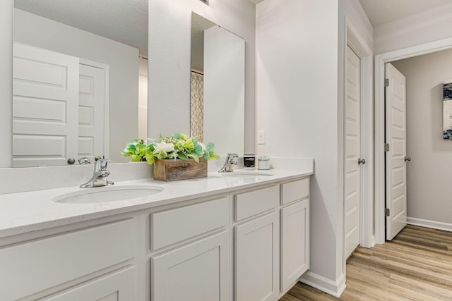 bathroom featuring double vanity, wood finished floors, a sink, and baseboards