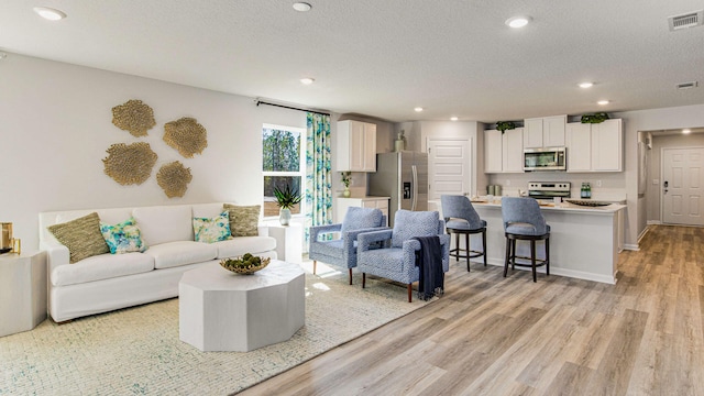 living room featuring light wood finished floors, recessed lighting, visible vents, a textured ceiling, and baseboards