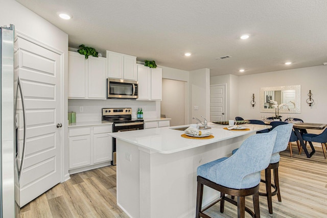 kitchen with a kitchen island with sink, stainless steel appliances, light countertops, white cabinetry, and a sink