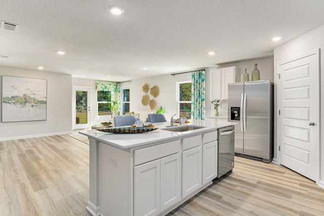 kitchen featuring stainless steel appliances, light countertops, white cabinets, a sink, and an island with sink