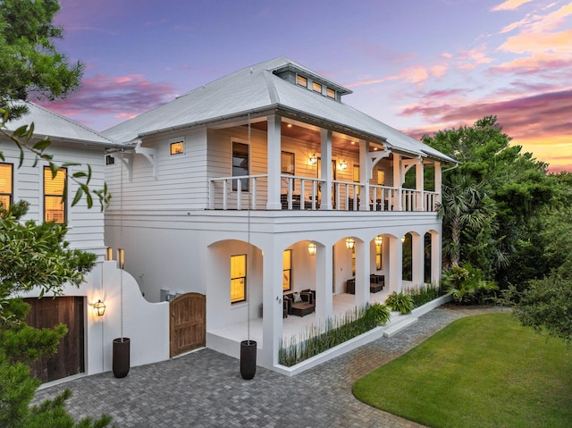 back house at dusk featuring a yard, a patio area, outdoor lounge area, and a balcony