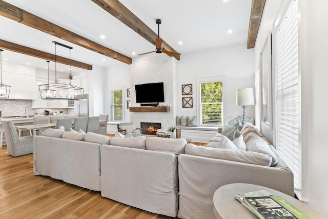 living room with sink, light hardwood / wood-style flooring, a large fireplace, ceiling fan, and beam ceiling