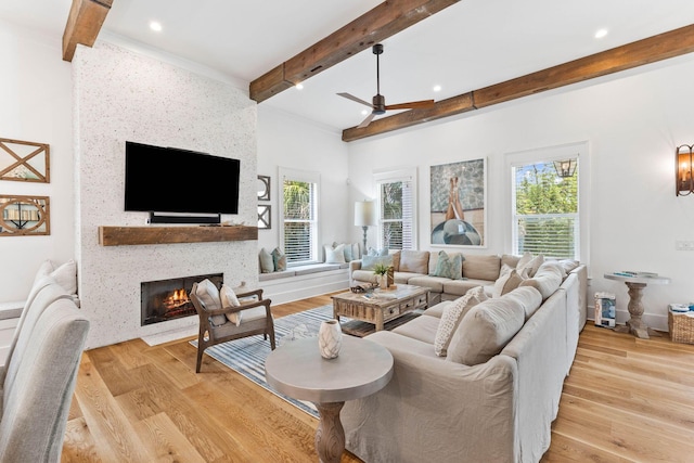 living room featuring beam ceiling, light hardwood / wood-style flooring, a large fireplace, and ceiling fan