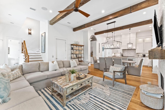 living room featuring beam ceiling, ceiling fan with notable chandelier, and light wood-type flooring