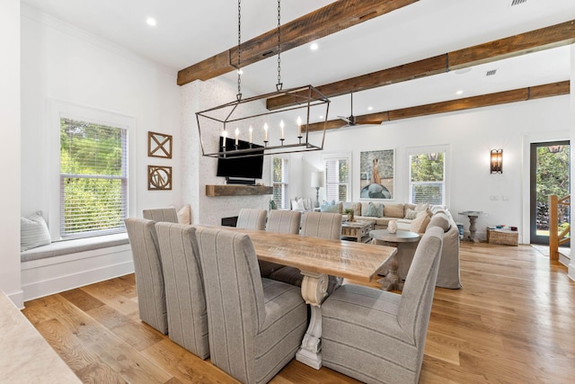 dining space with a large fireplace, a healthy amount of sunlight, beam ceiling, and light hardwood / wood-style flooring