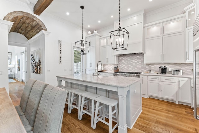 kitchen featuring decorative light fixtures, sink, white cabinets, a center island with sink, and light hardwood / wood-style flooring