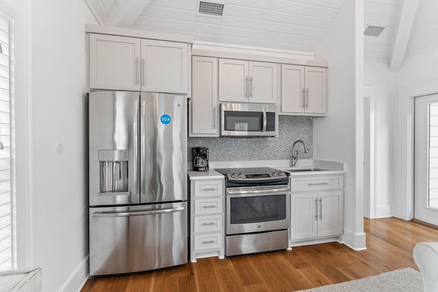 kitchen with appliances with stainless steel finishes, sink, vaulted ceiling with beams, backsplash, and hardwood / wood-style flooring