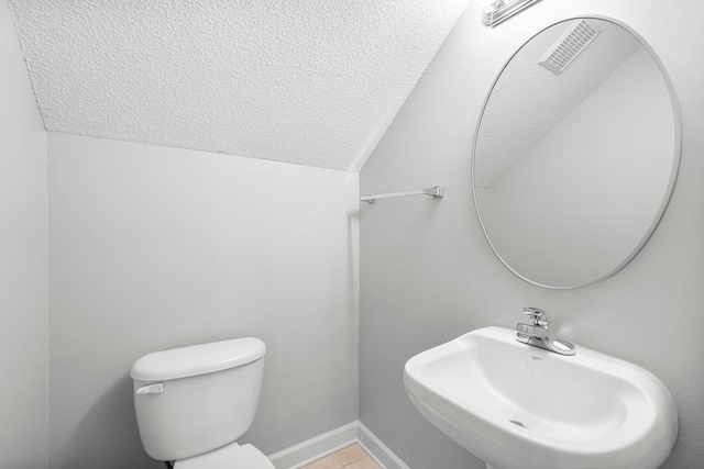 bathroom with lofted ceiling, toilet, a textured ceiling, and sink