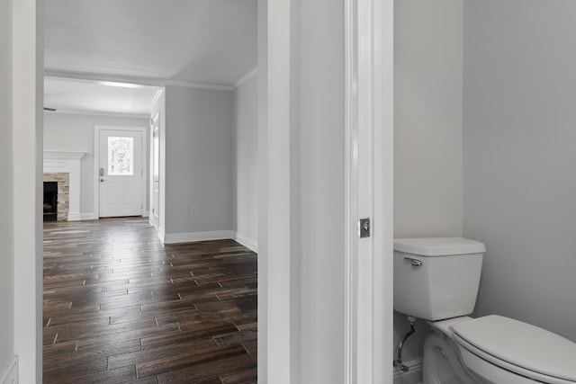 bathroom with toilet, a stone fireplace, hardwood / wood-style floors, and crown molding