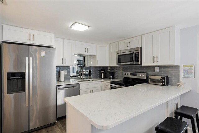 kitchen with dark hardwood / wood-style flooring, white cabinets, decorative backsplash, appliances with stainless steel finishes, and kitchen peninsula