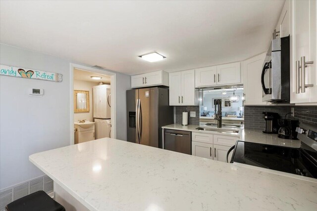 kitchen with white cabinetry, tasteful backsplash, washer / dryer, light stone countertops, and appliances with stainless steel finishes