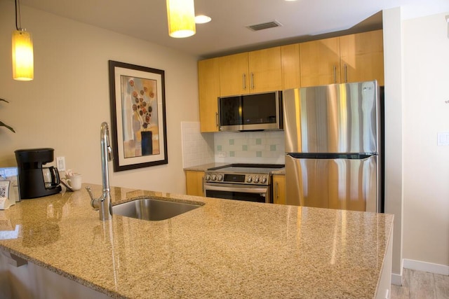 kitchen featuring light stone countertops, kitchen peninsula, decorative backsplash, stainless steel appliances, and pendant lighting