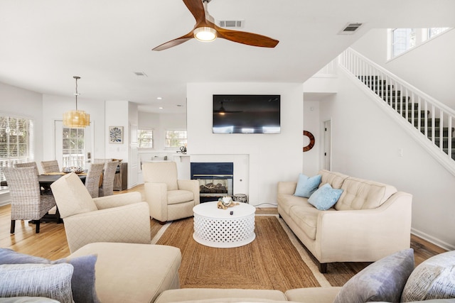 living room featuring ceiling fan, a healthy amount of sunlight, a multi sided fireplace, and light hardwood / wood-style flooring