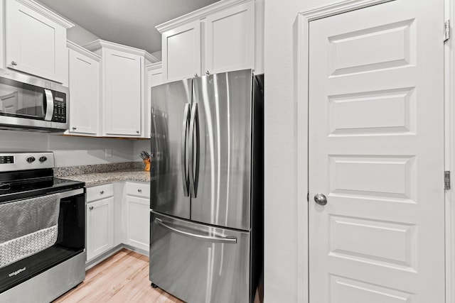 kitchen with white cabinets, appliances with stainless steel finishes, light hardwood / wood-style floors, and light stone counters