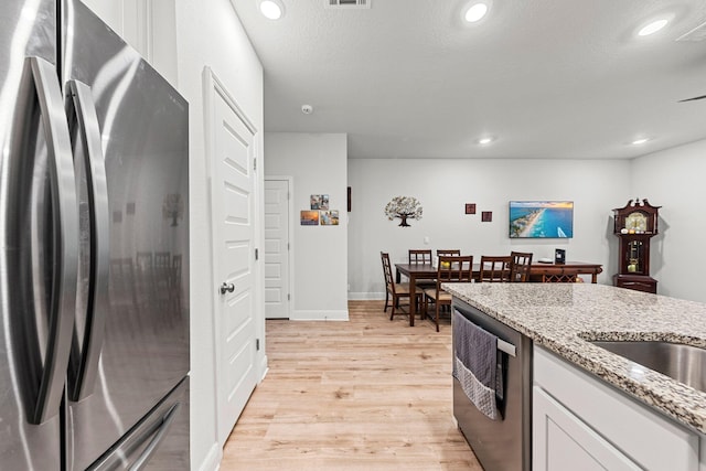 kitchen with light hardwood / wood-style floors, light stone countertops, white cabinetry, and stainless steel appliances