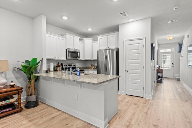 kitchen with sink, kitchen peninsula, light stone counters, white cabinetry, and stainless steel appliances