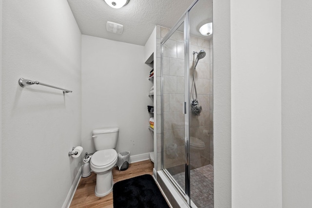 bathroom with toilet, a shower with door, a textured ceiling, and hardwood / wood-style flooring