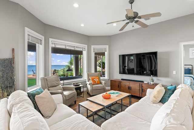 living room with ceiling fan, plenty of natural light, wood-type flooring, and a water view