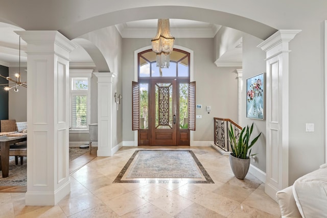 foyer entrance featuring ornate columns, ornamental molding, and a chandelier